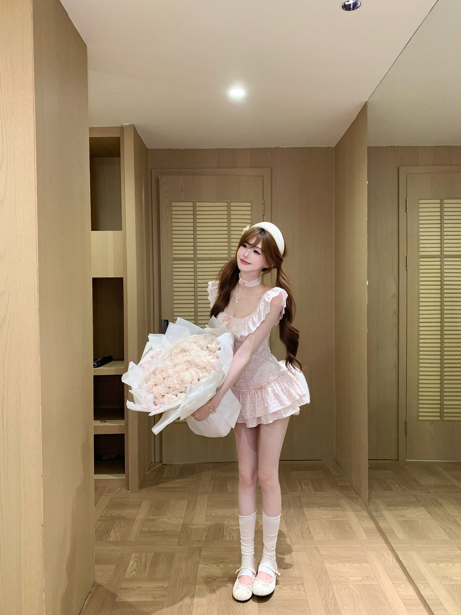 Person in a pink dress outfit holding a bouquet of flowers in a room with wooden flooring and beige walls.