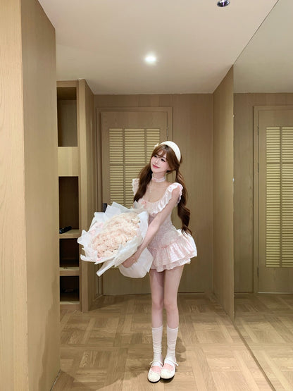 Person in a pink dress outfit holding a bouquet of flowers in a room with wooden flooring and beige walls.