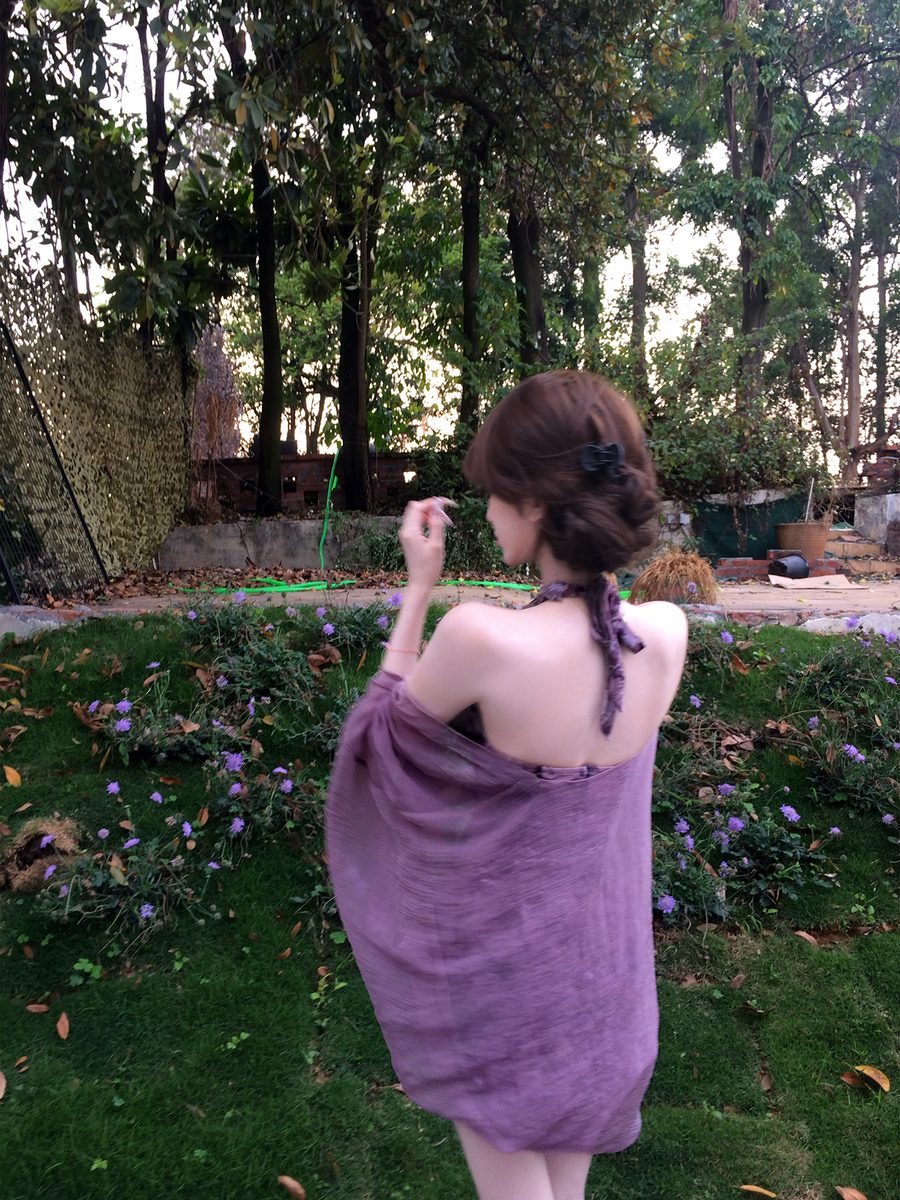 Woman in a purple dress standing in a garden with trees and plants in the background
