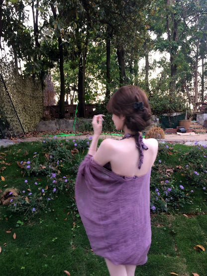 Woman in a purple dress standing in a garden with trees and plants in the background