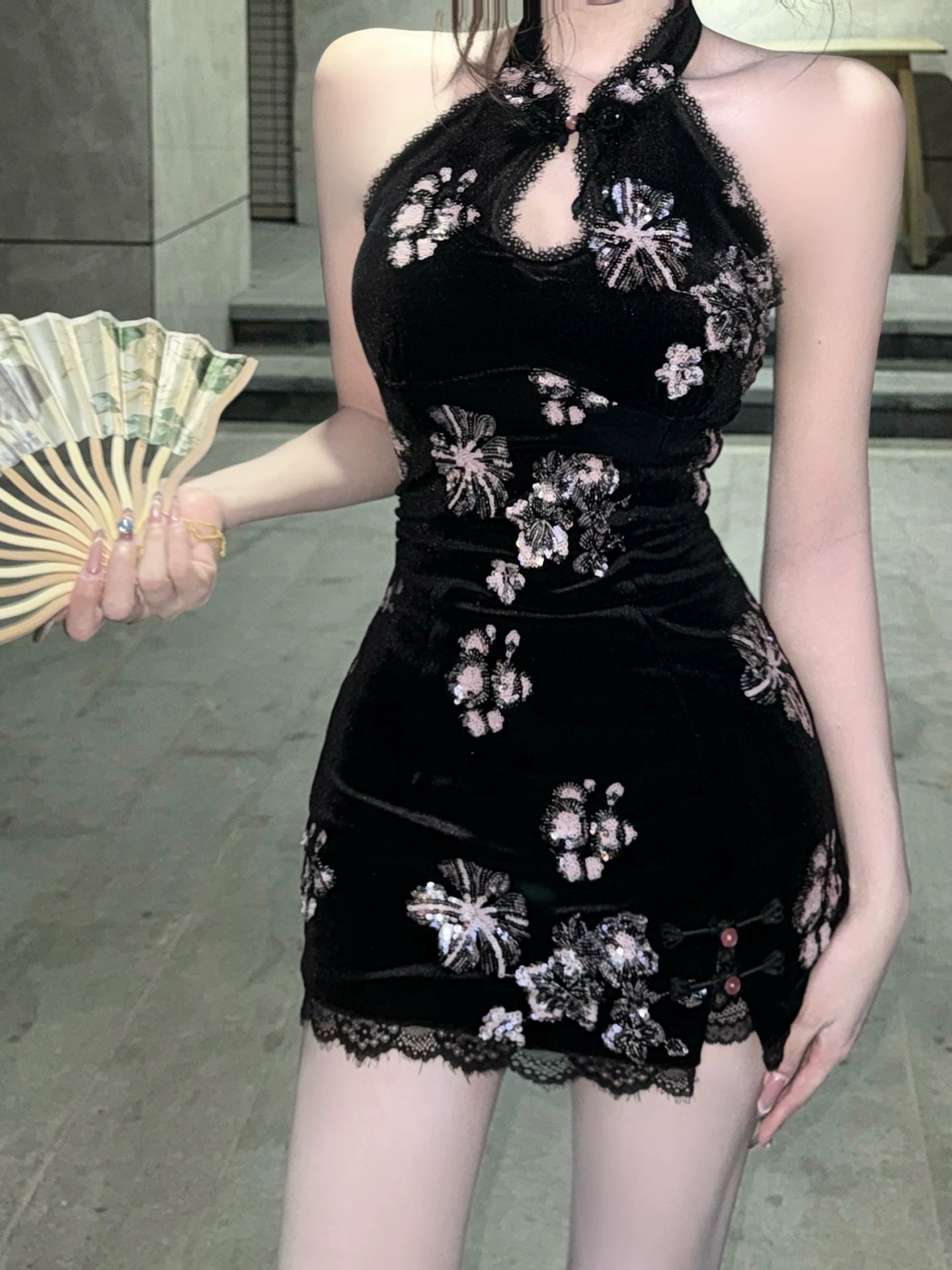 Woman wearing a black dress with floral embroidery, holding a fan.