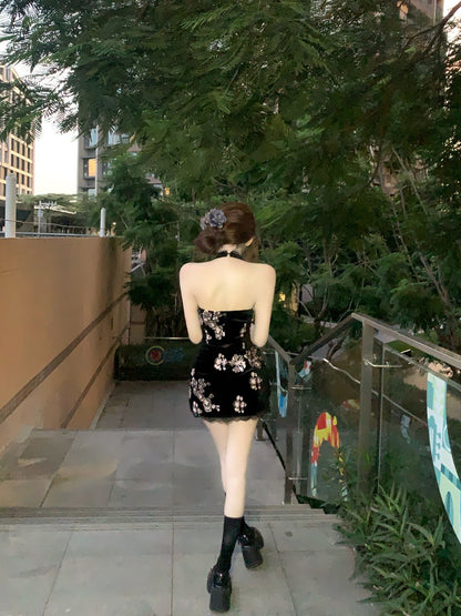 Woman in a black floral dress walking on a sidewalk with greenery and buildings in the background