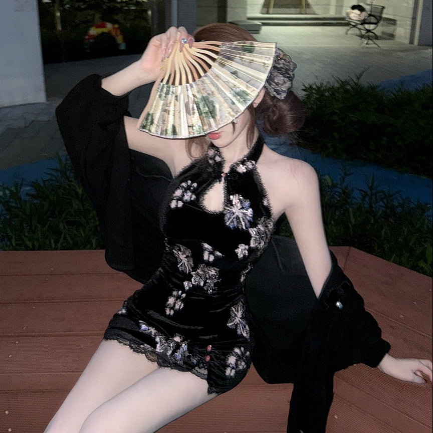 Woman in a black outfit with floral embroidery holding a fan outdoors.