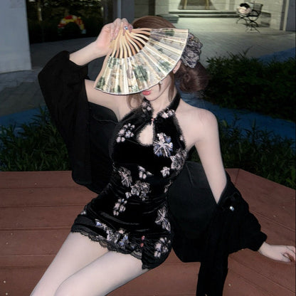 Woman in a black outfit with floral embroidery holding a fan outdoors.
