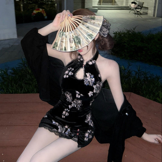 Woman in a black outfit with floral embroidery holding a fan outdoors.