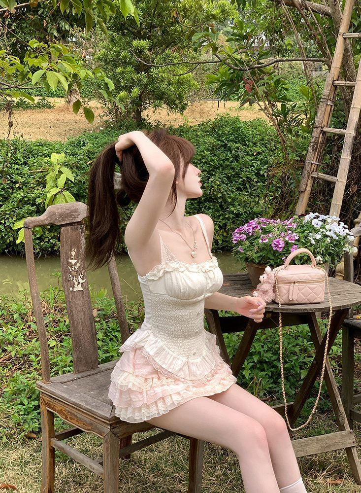 Woman in a white lace dress sitting outdoors with flowers and a chair.