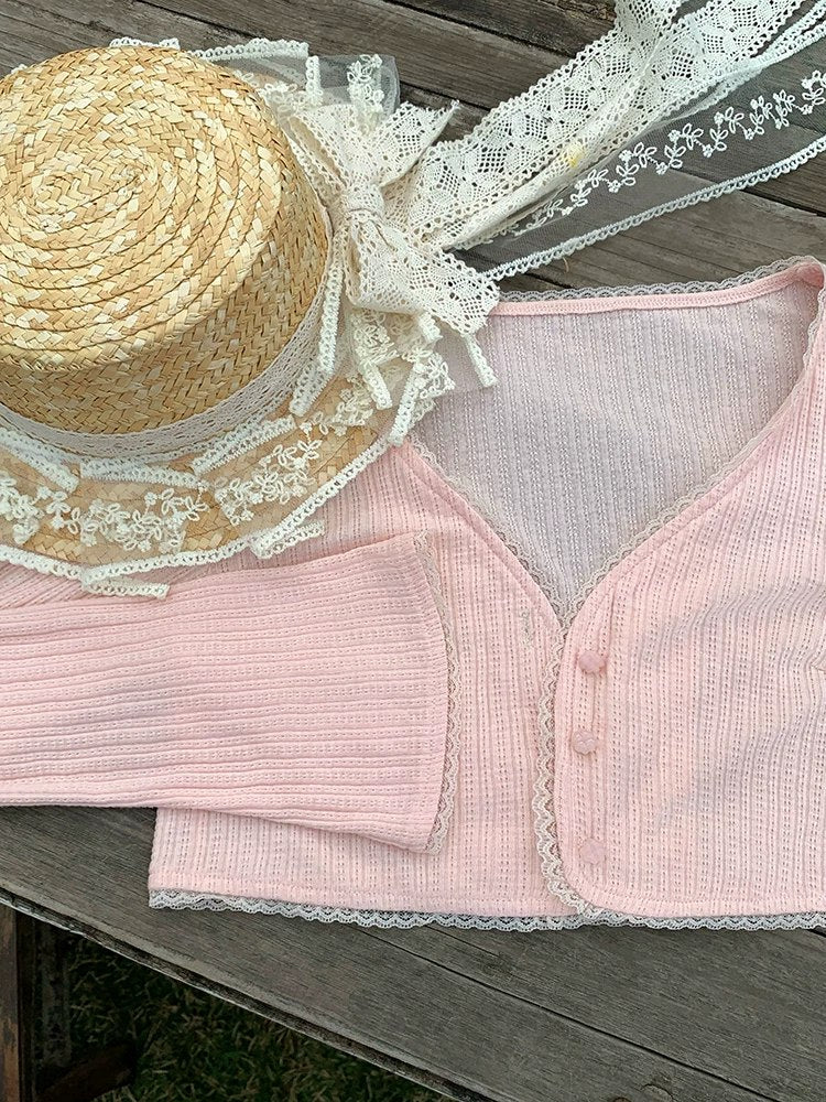 Straw hat with lace and pink ribbed cardigan on a wooden surface