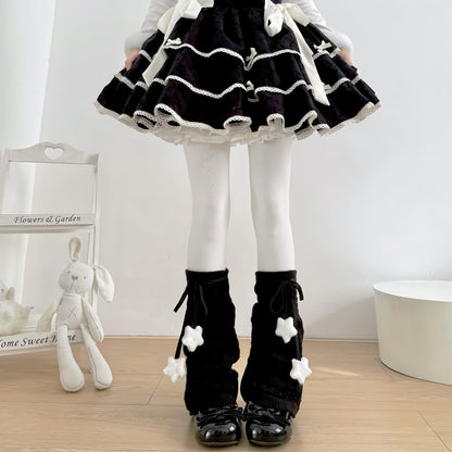 Person wearing a black and white outfit with a skirt and leg warmers, standing indoors.