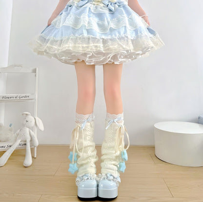 A person wearing a light blue and cream Lolita-style ruffled skirt with matching cream lace socks and light blue platform shoes, standing indoors on a wood floor.