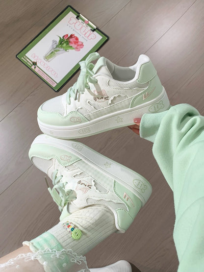 Pair of light green sneakers with floral patterns on a wooden floor.