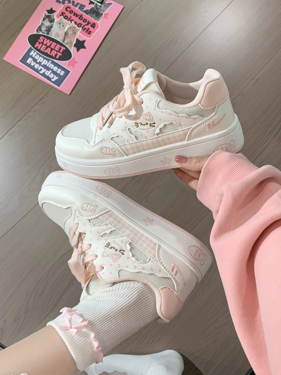 White sneakers with pink accents held by a person on a wooden floor.