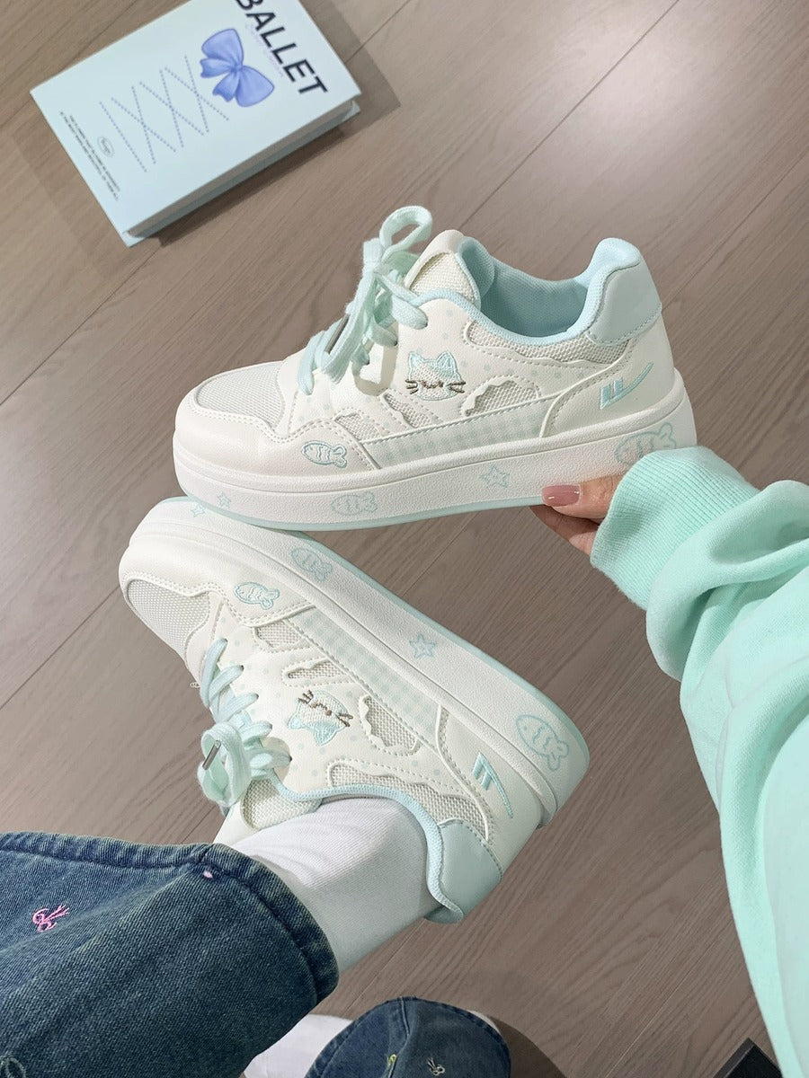 White sneakers with light blue accents held by a person on a wooden floor.