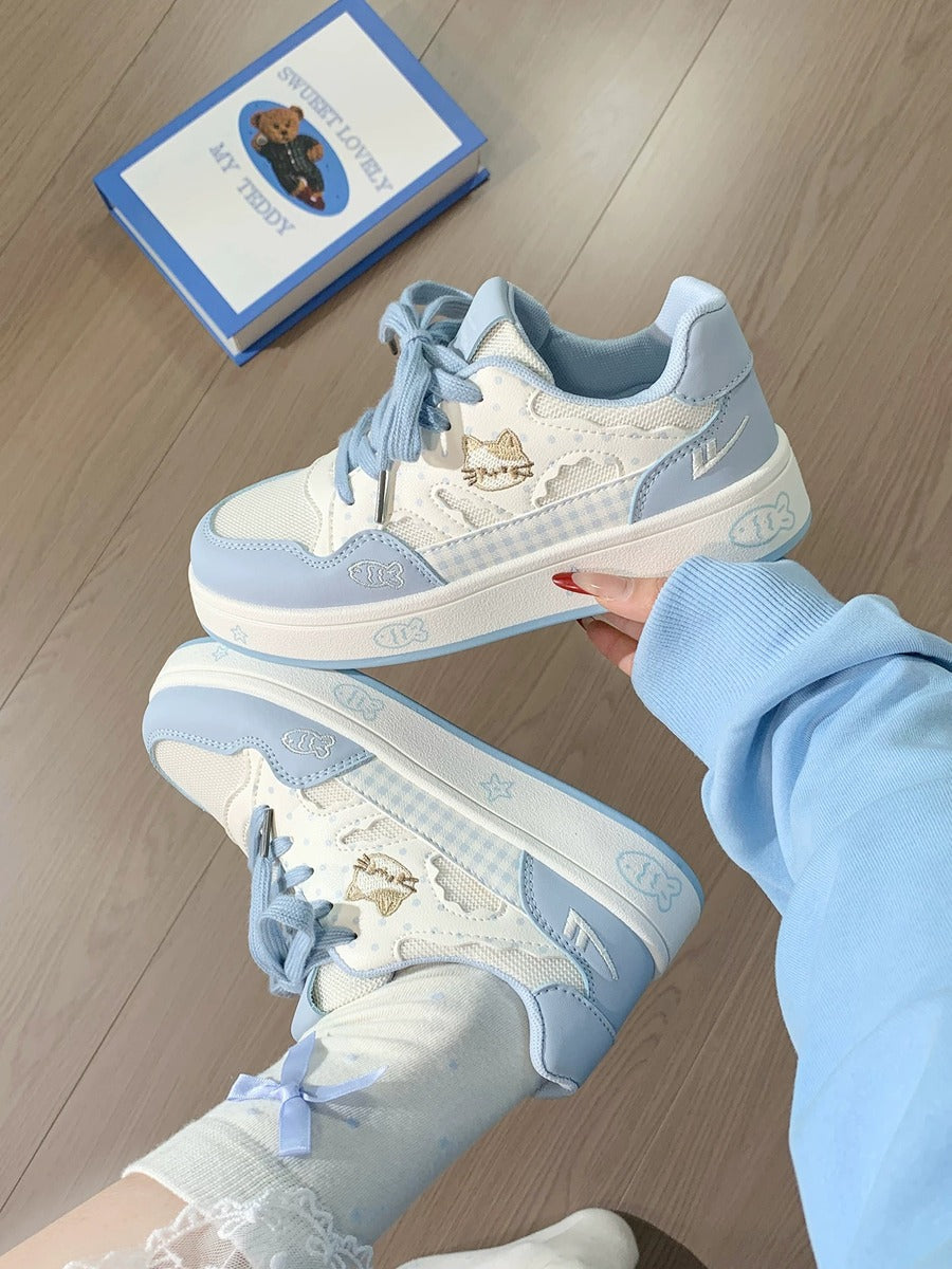 Light blue and white sneakers held by a person wearing a matching outfit on a wooden floor.