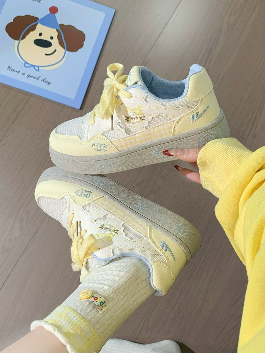 Yellow sneakers with white soles held by a person on a wooden floor.