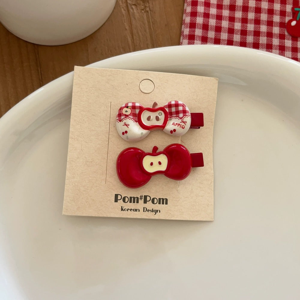 Two red and white apple-shaped hair clips on a 'Pom Pom Korean Design' card.