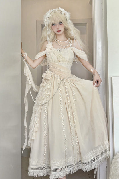 A woman wearing a cream-colored off-the-shoulder Lolita dress with lace details, a matching floral headpiece, and pearl necklaces, posing in front of a neutral indoor background.