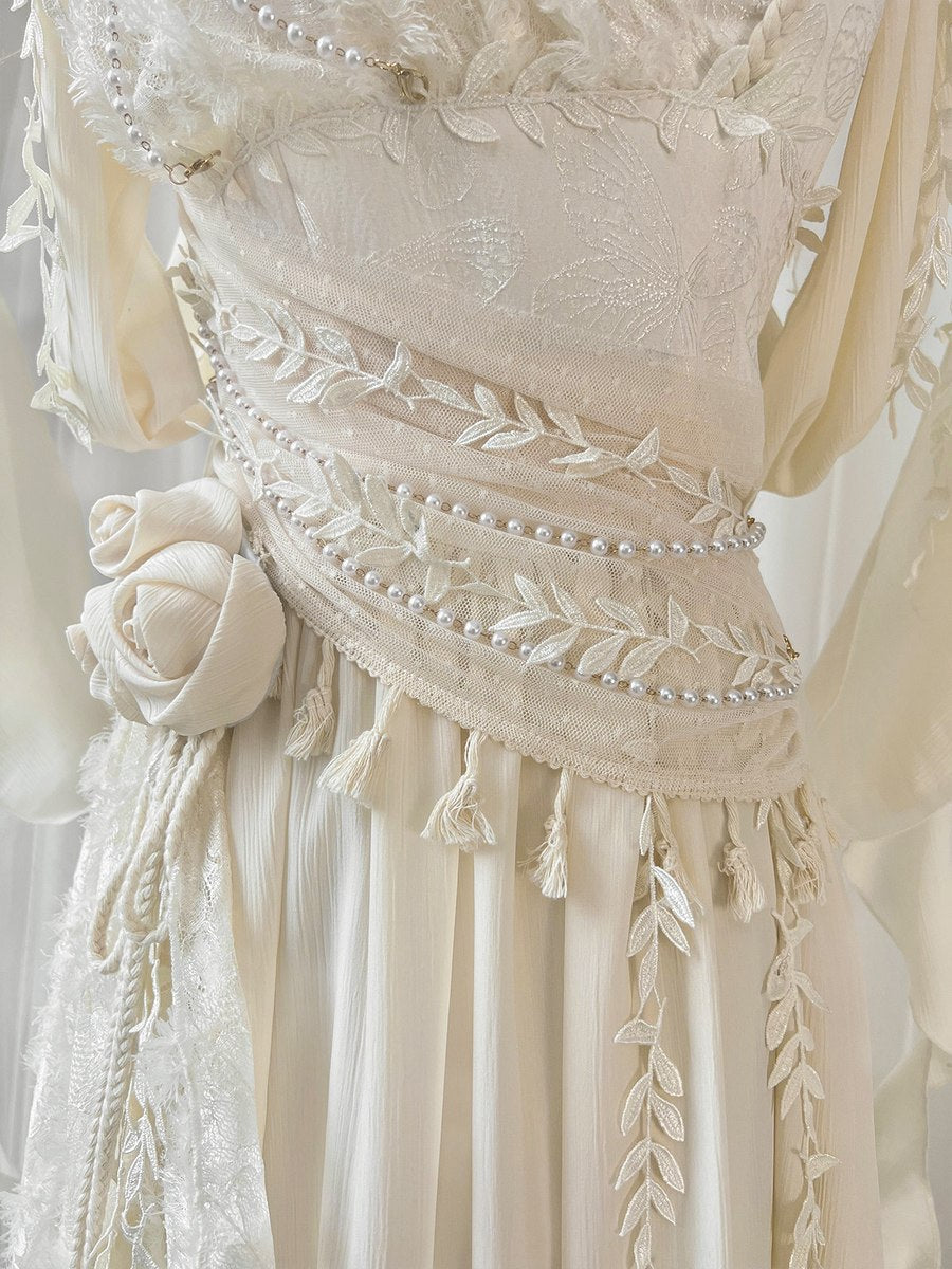 Close-up of a cream-colored embroidered dress featuring intricate floral lace, delicate bead trim, tassels, and a matching fabric rose detail on the skirt.