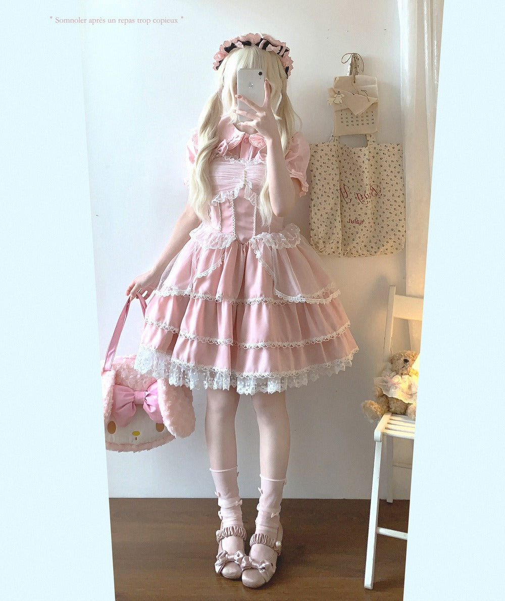 Person wearing a pink Lolita-style dress in a room with a white wall and wooden floor.