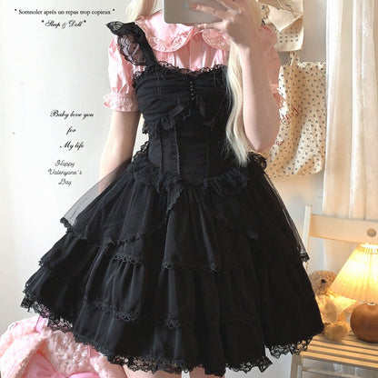 Person wearing a black lace dress with a pink top, standing in a room with a lamp and window.