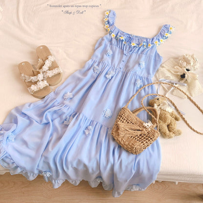 Blue dress with floral details, sandals, straw bag, and teddy bear on a wooden surface.