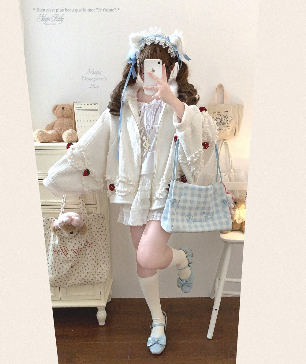 Person in a cute strawberry jacket with a teddy bear and decorative items in the background