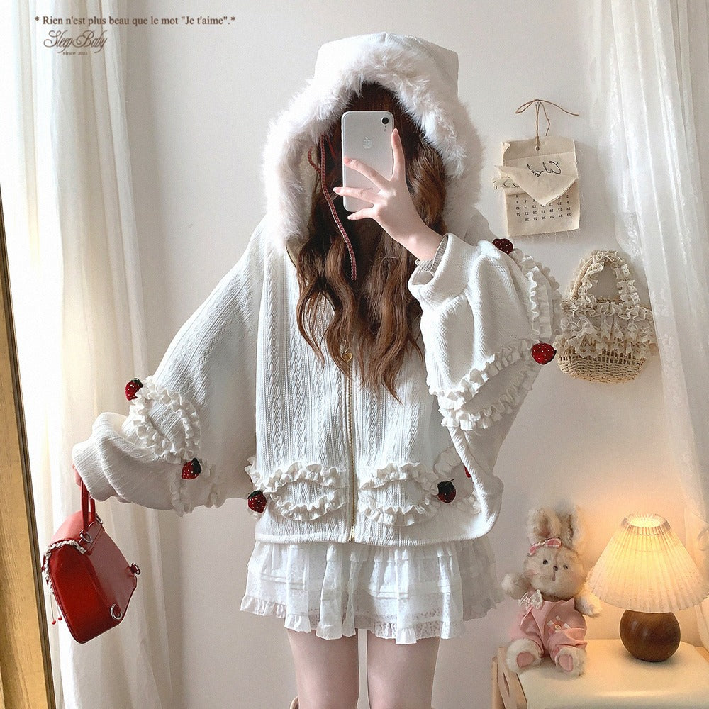 Person wearing a white strawberry jacket with red accents in a room with a lamp and teddy bear.