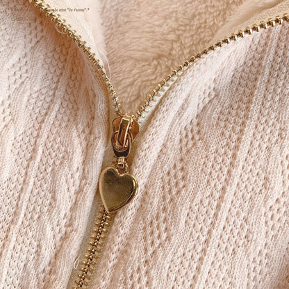 Close-up of a gold zipper with a heart-shaped pull on a textured beige background