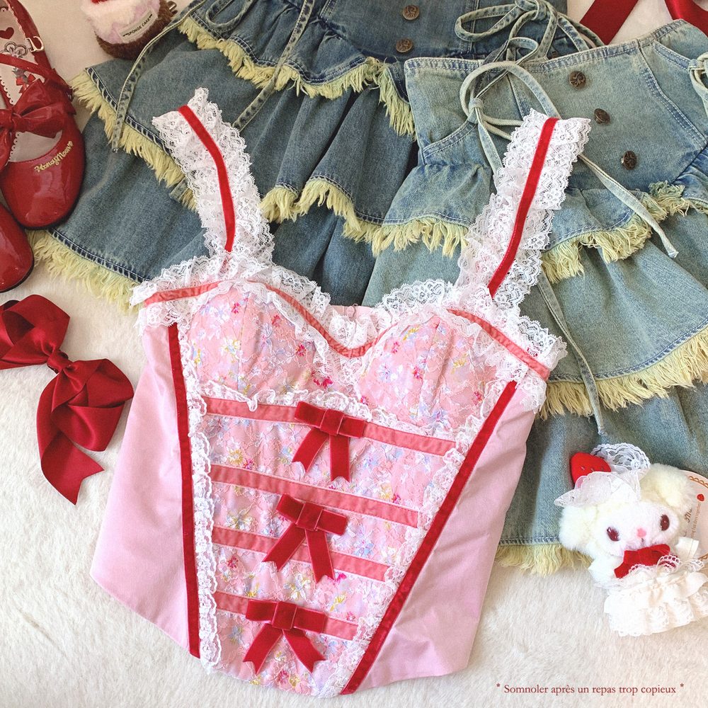Pink lace baby outfit with red accents on a white surface, surrounded by denim dress and red shoes.
