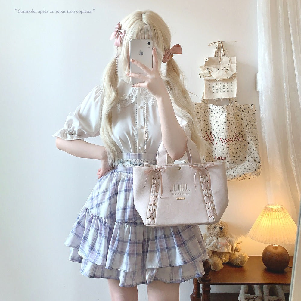 Person in a white blouse and plaid skirt holding a pink handbag with a mirror.