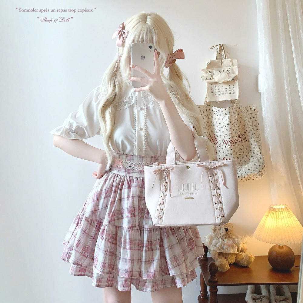 Person in a white blouse and plaid skirt holding a pink handbag, with a lamp and decorative items in the background.