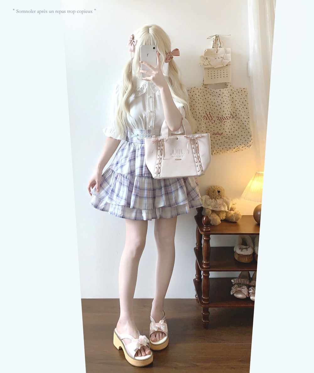 Person wearing a white blouse and plaid skirt with a handbag in a room.