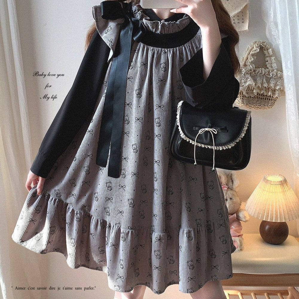 Person wearing a gray dress with black patterns and holding a matching handbag in a softly lit room.