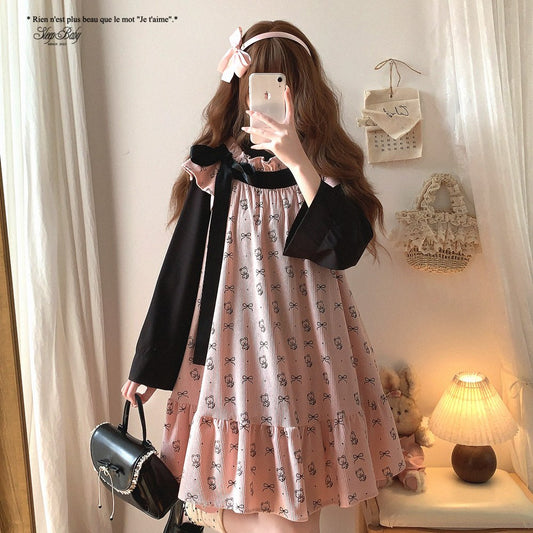 Woman taking a mirror selfie wearing a black and pink dress with a bow, holding a black handbag.