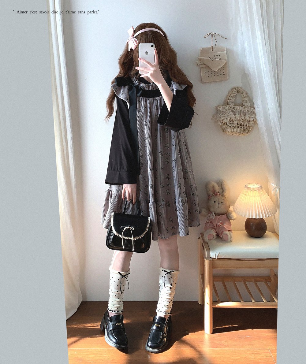 Person taking a mirror selfie wearing a black and gray dress with a small handbag in a room.