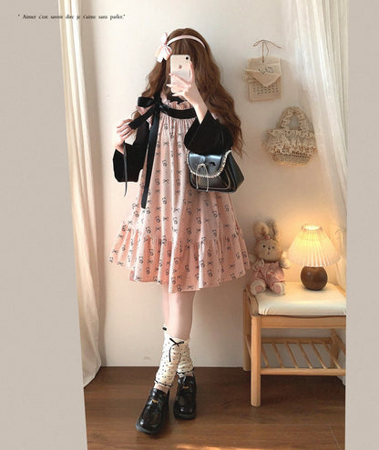 Woman taking a mirror selfie wearing a floral dress and black shoes in a room with a teddy bear and lamp.