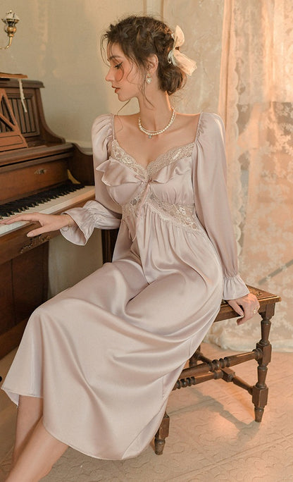 A woman wearing a long-sleeve satin nightgown with lace trim sits on a wooden bench next to a vintage piano in a softly lit room.
