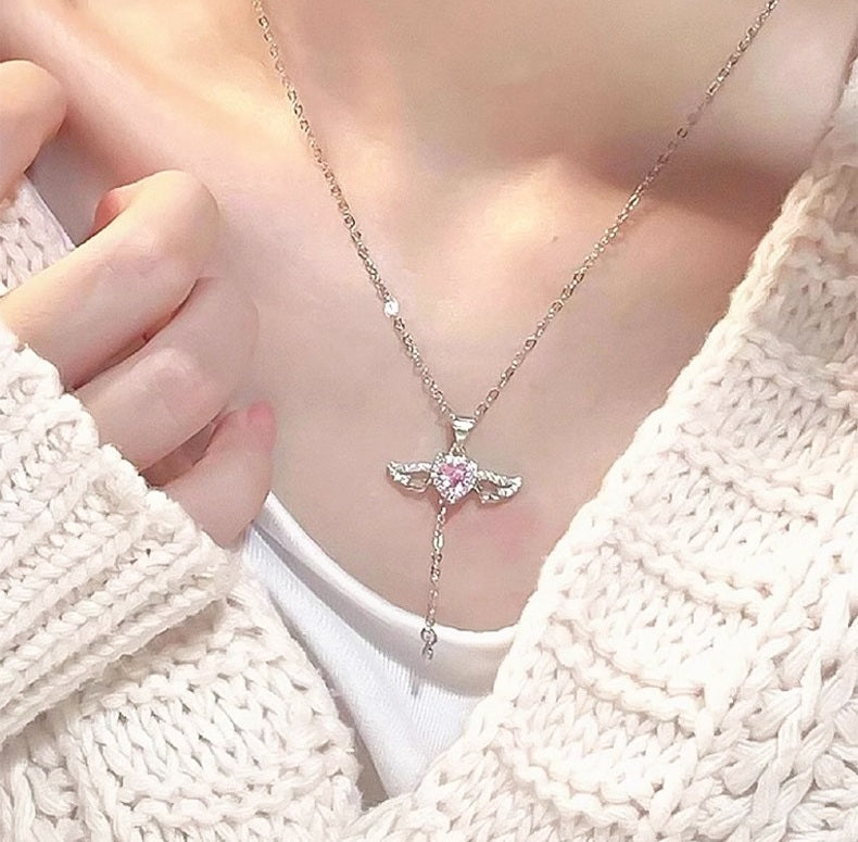 Necklace with a pink heart pendant worn by a person in a white sweater.