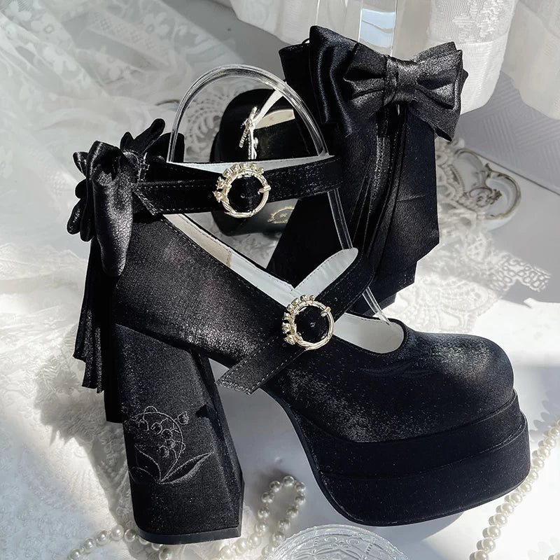 Black platform shoes with decorative bows and straps on a white textured background