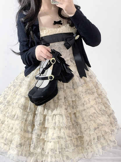 Person wearing a layered dress with a black bow and holding a black shoe.