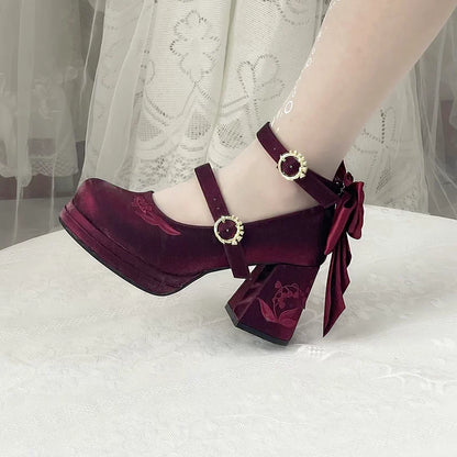Maroon high-heeled shoes with bow detail on a white surface