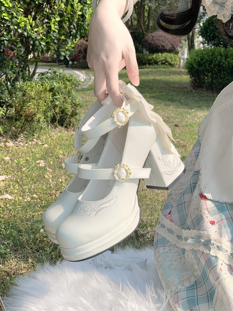 White shoes with decorative buckles held by a hand outdoors.