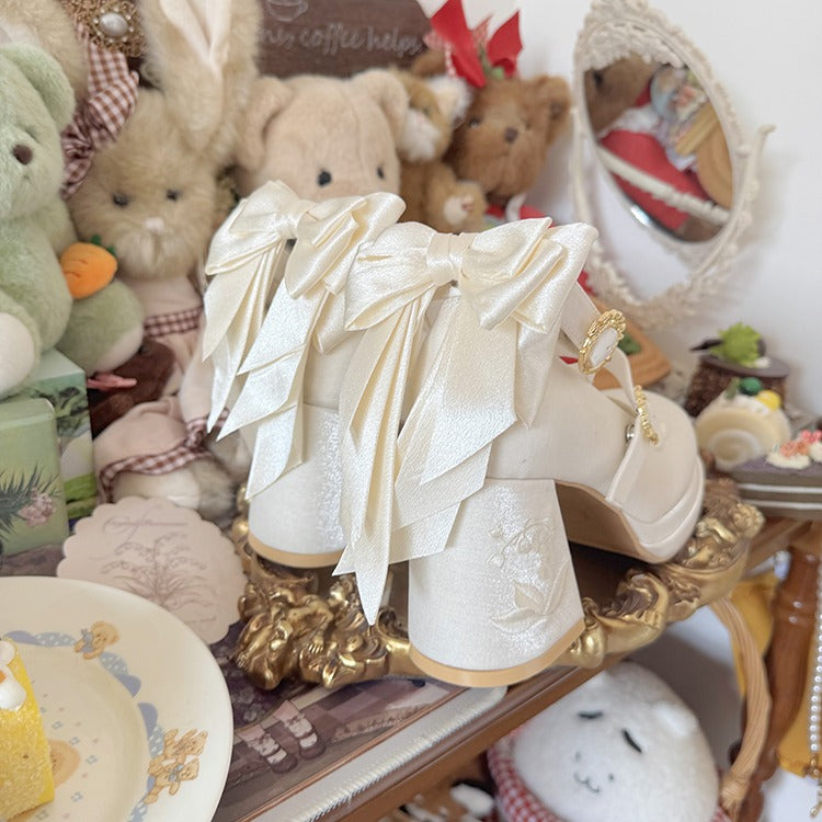 Pair of white high-heeled shoes with gold accents on a decorative surface with teddy bears and other items in the background.