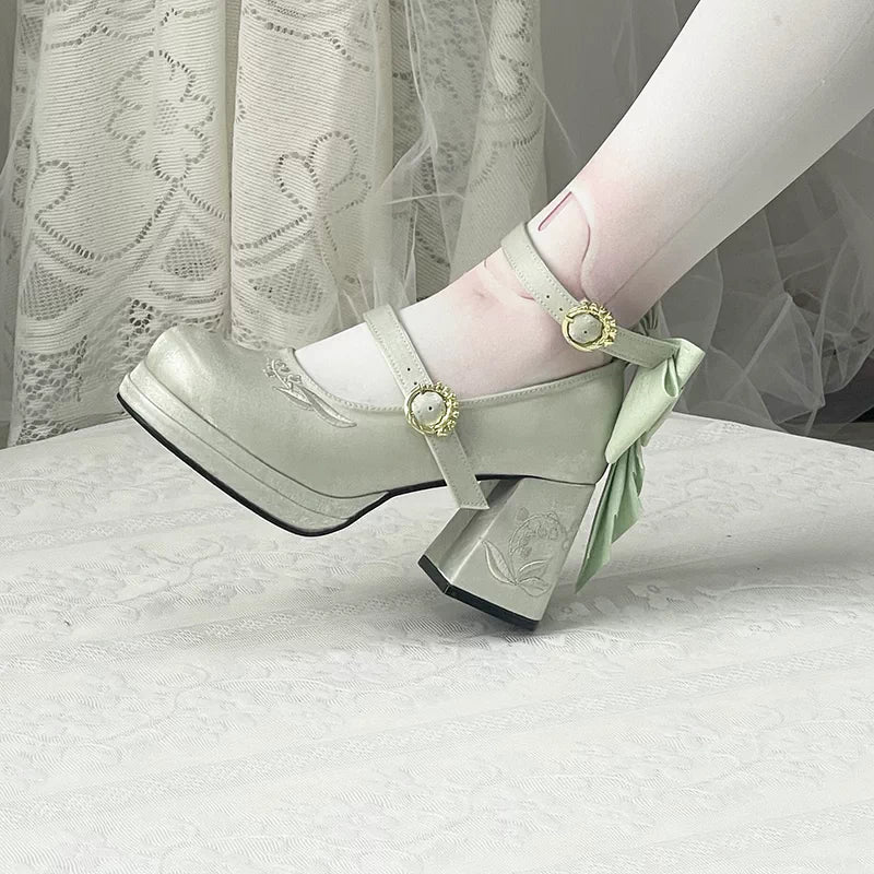 Light green high-heeled shoes with decorative straps on a white surface.