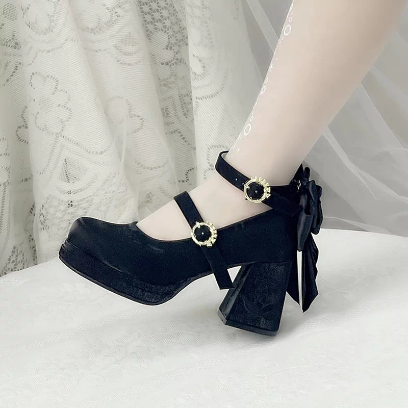Black high-heeled shoes with decorative buckles worn by a person on a white surface.