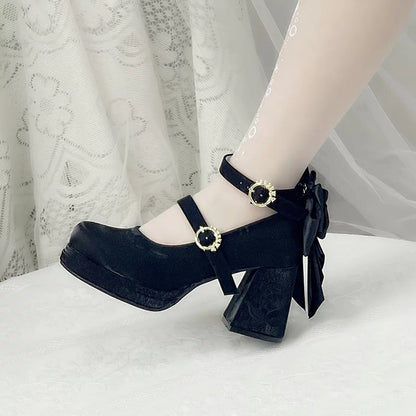Black high-heeled shoes with decorative buckles worn by a person on a white surface.
