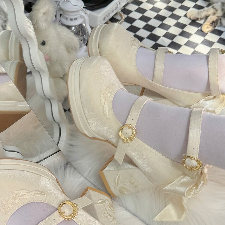 Pair of cream-colored high-heeled shoes with decorative ribbons on a checkered floor.