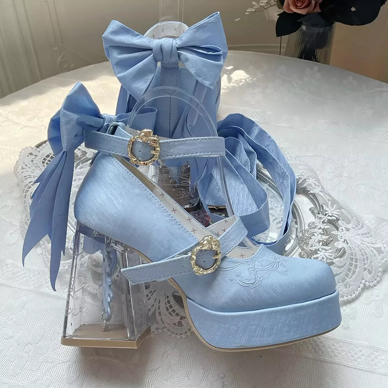Light blue high-heeled shoes with decorative bows on a white lace tablecloth.