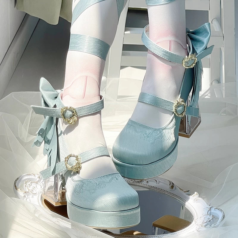 Light blue high-heeled shoes with decorative straps and bows on a reflective surface.