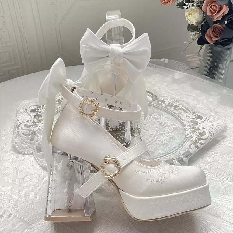 White high-heeled shoes with decorative straps and a bow on a white surface.