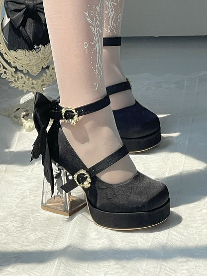 Black platform shoes with gold buckles and bows on a white background